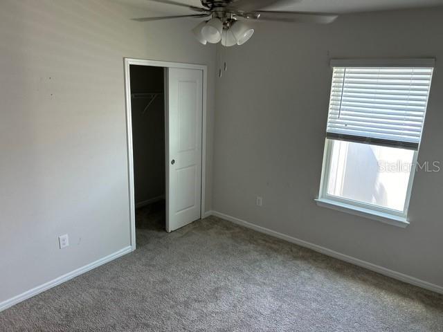 unfurnished bedroom featuring carpet flooring, baseboards, a closet, and a ceiling fan