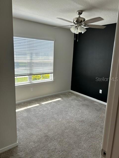 unfurnished room with ceiling fan, baseboards, carpet flooring, and a textured ceiling