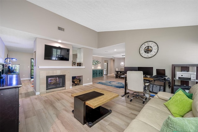 living room with light wood-type flooring, a textured ceiling, vaulted ceiling, and a tiled fireplace