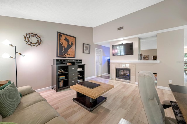 living room with light hardwood / wood-style flooring, lofted ceiling, a tiled fireplace, and a textured ceiling