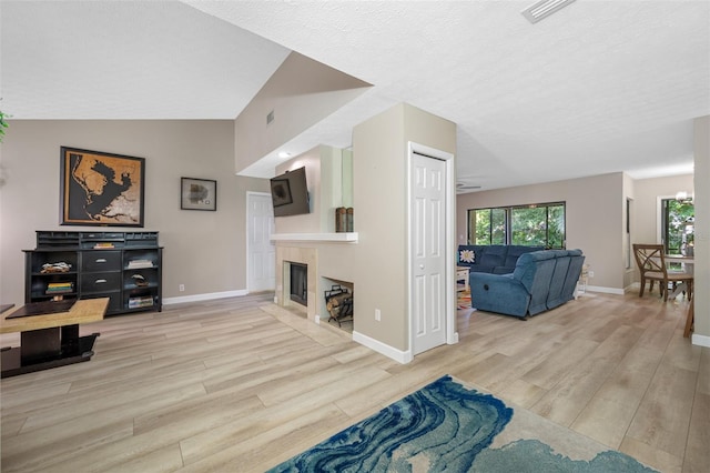 living room with light wood-type flooring, lofted ceiling, a textured ceiling, and a tiled fireplace