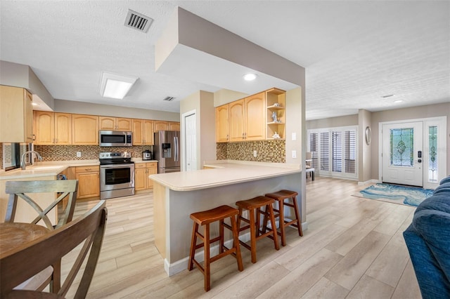 kitchen featuring a textured ceiling, tasteful backsplash, kitchen peninsula, light hardwood / wood-style flooring, and appliances with stainless steel finishes