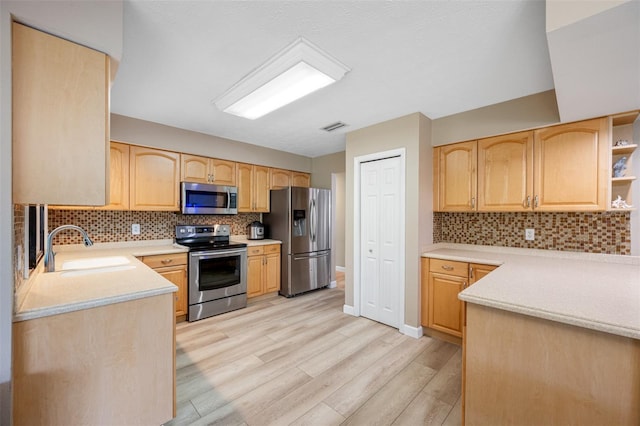 kitchen featuring sink, backsplash, stainless steel appliances, light brown cabinetry, and light wood-type flooring