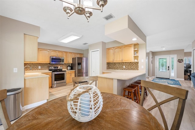 kitchen featuring light wood-type flooring, kitchen peninsula, stainless steel appliances, backsplash, and light brown cabinetry