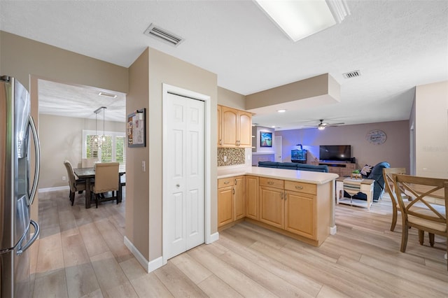 kitchen with stainless steel fridge, kitchen peninsula, pendant lighting, light brown cabinetry, and light hardwood / wood-style flooring