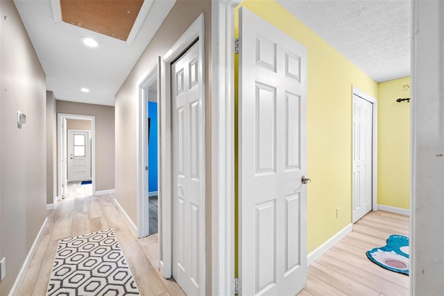 hall featuring light wood-type flooring and a textured ceiling