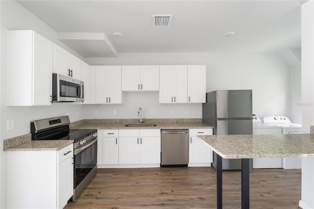 kitchen with washing machine and dryer, white cabinetry, stainless steel appliances, dark hardwood / wood-style floors, and sink