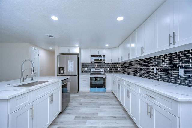 kitchen with appliances with stainless steel finishes, sink, light hardwood / wood-style floors, white cabinets, and light stone counters