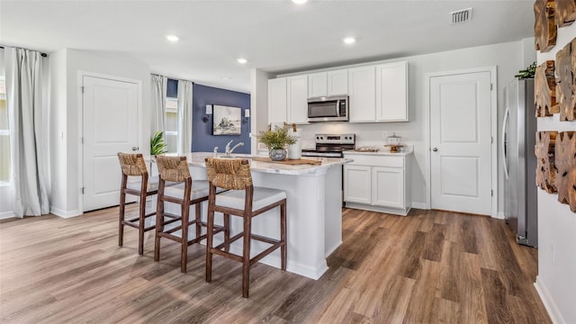 kitchen with white cabinets, a center island with sink, hardwood / wood-style flooring, stainless steel appliances, and a kitchen bar