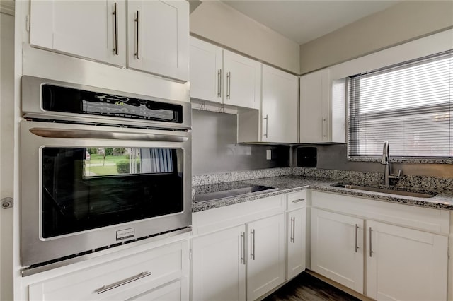 kitchen featuring light stone countertops, oven, sink, white cabinetry, and black electric stovetop