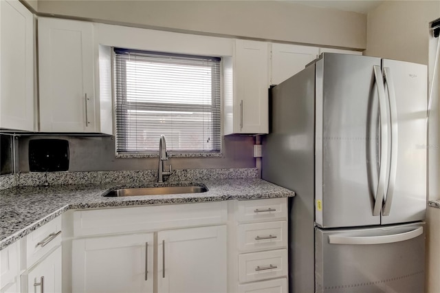 kitchen featuring light stone countertops, stainless steel refrigerator, sink, and white cabinetry