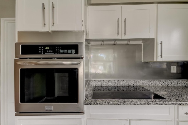 kitchen with light stone counters, white cabinets, oven, and black electric stovetop