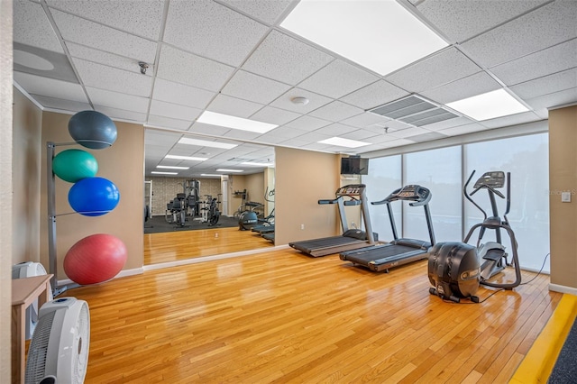 gym featuring a paneled ceiling, hardwood / wood-style floors, and heating unit