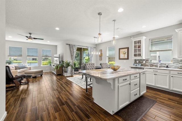 kitchen with dark hardwood / wood-style flooring, a kitchen breakfast bar, a kitchen island, white cabinetry, and decorative light fixtures