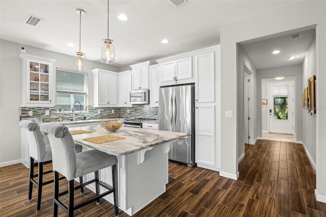 kitchen with appliances with stainless steel finishes, hanging light fixtures, a kitchen island, white cabinets, and dark hardwood / wood-style flooring