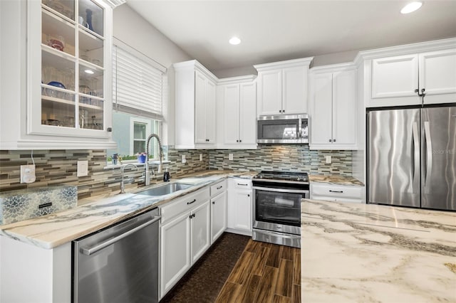 kitchen with stainless steel appliances, white cabinetry, sink, and light stone counters