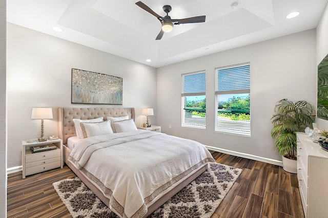 bedroom with dark wood-type flooring, ceiling fan, and a tray ceiling