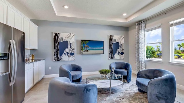 living area with a tray ceiling, a textured ceiling, and light tile patterned floors