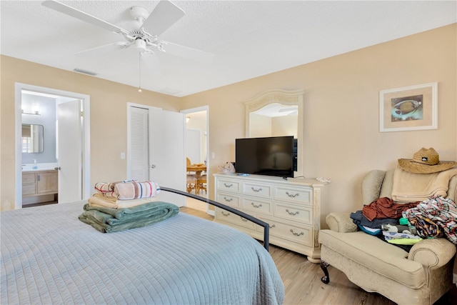 bedroom featuring light wood-type flooring, a textured ceiling, a closet, ceiling fan, and connected bathroom