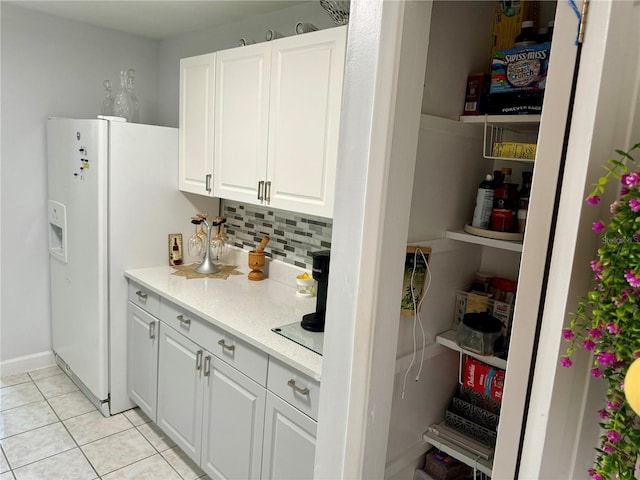 interior space featuring light stone countertops, light tile patterned floors, tasteful backsplash, white refrigerator with ice dispenser, and white cabinets