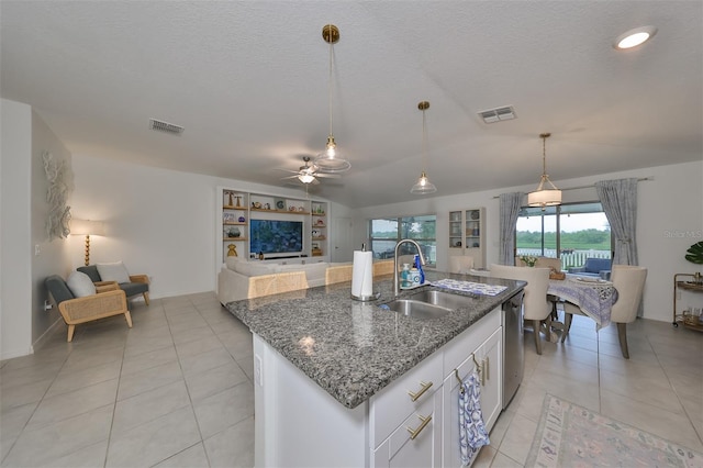 kitchen featuring decorative light fixtures, a kitchen island with sink, dark stone counters, white cabinets, and sink