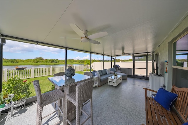 sunroom with ceiling fan and a water view