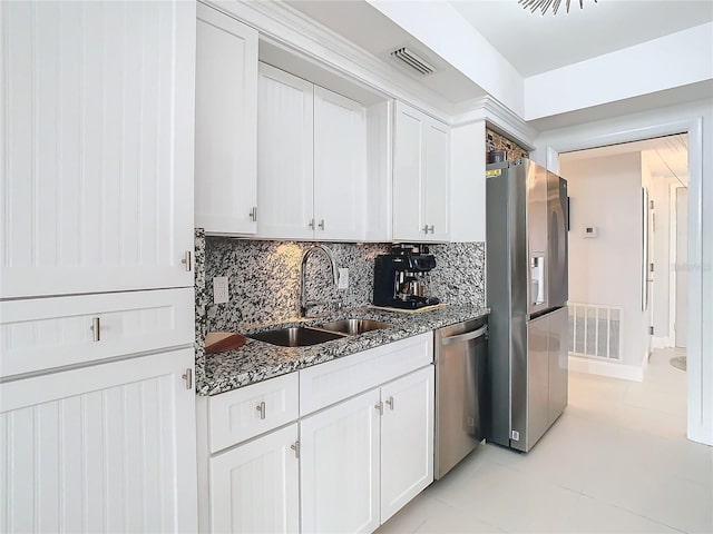 kitchen with sink, appliances with stainless steel finishes, dark stone countertops, light tile patterned floors, and white cabinets