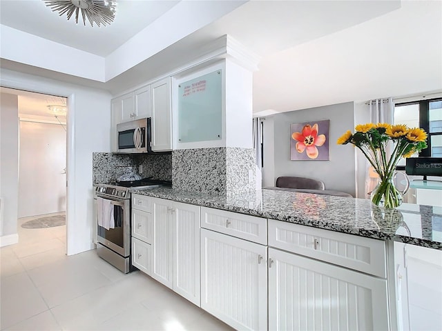 kitchen featuring stainless steel appliances, white cabinets, light tile patterned floors, backsplash, and dark stone countertops