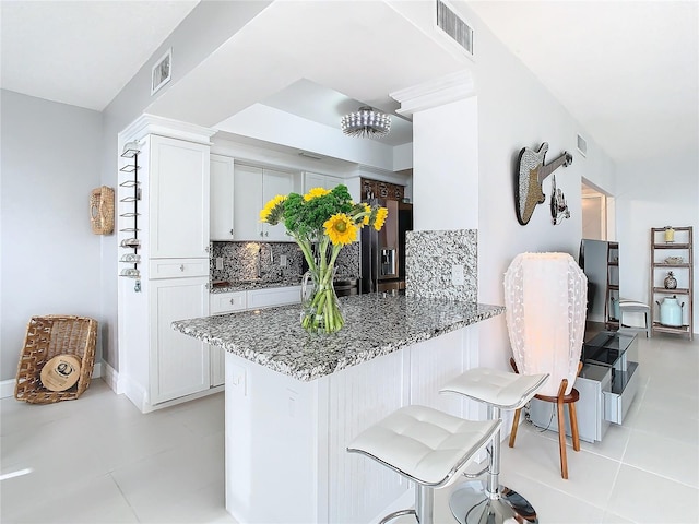 kitchen featuring kitchen peninsula, light tile patterned flooring, a breakfast bar, white cabinetry, and dark stone countertops