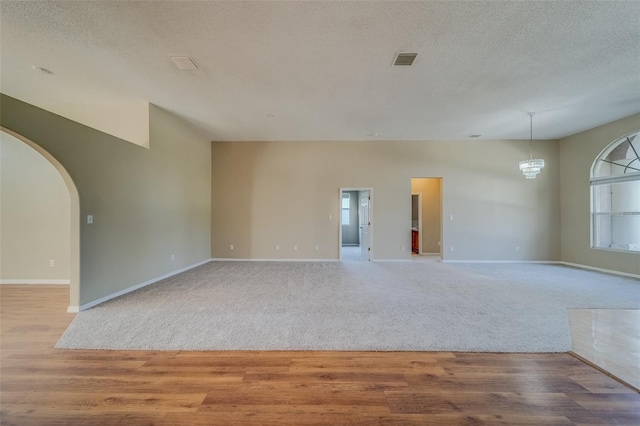 unfurnished room featuring a notable chandelier, light wood-type flooring, and a textured ceiling