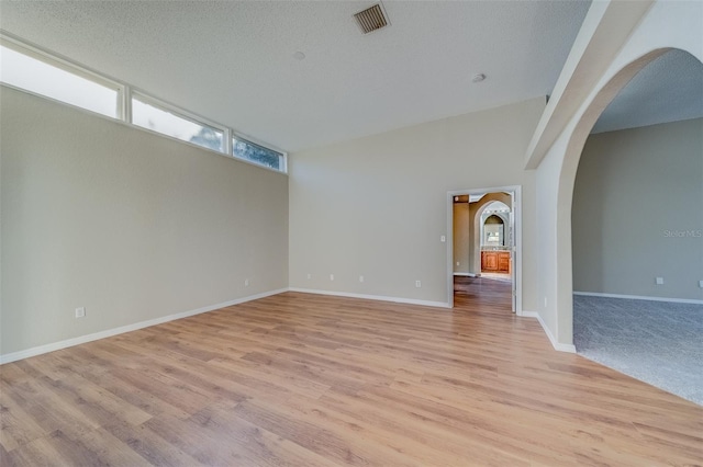 unfurnished room featuring a textured ceiling, vaulted ceiling, and light hardwood / wood-style flooring