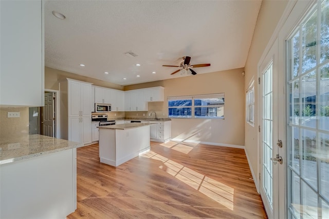 kitchen with white cabinets, ceiling fan, light stone countertops, light wood-type flooring, and stainless steel appliances