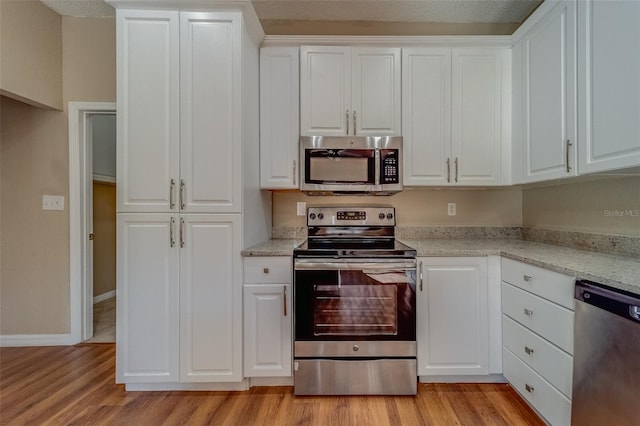 kitchen with light wood-type flooring, stainless steel appliances, white cabinetry, and light stone counters