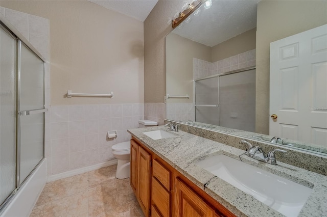 full bathroom featuring combined bath / shower with glass door, vanity, a textured ceiling, tile patterned flooring, and toilet