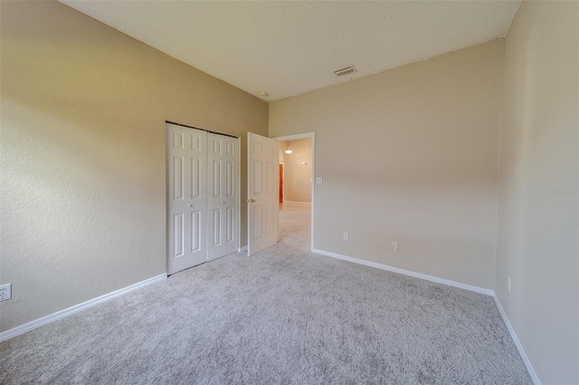 unfurnished bedroom featuring light carpet, a textured ceiling, and a closet