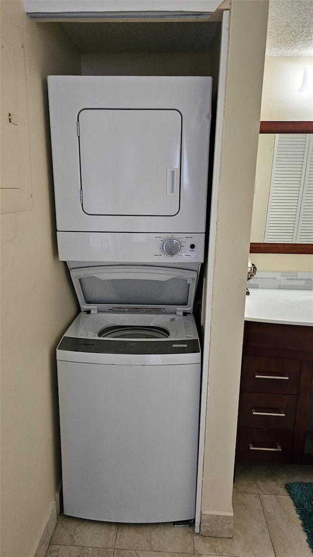 clothes washing area with stacked washer and clothes dryer, a textured ceiling, and light tile patterned floors