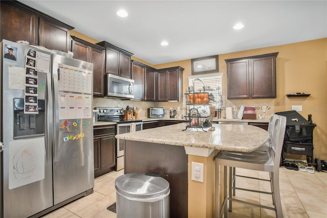 kitchen featuring dark brown cabinetry, a kitchen island, light tile patterned floors, and stainless steel appliances