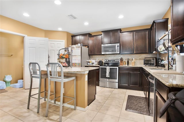 kitchen with light stone countertops, a breakfast bar area, stainless steel appliances, and a kitchen island