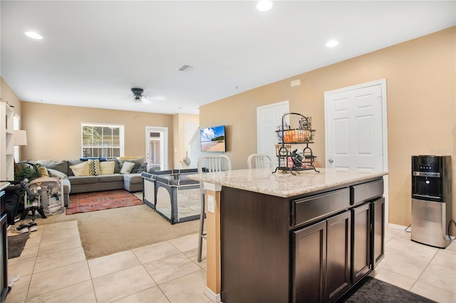 kitchen featuring dark brown cabinets, light stone counters, a kitchen island, light tile patterned floors, and ceiling fan