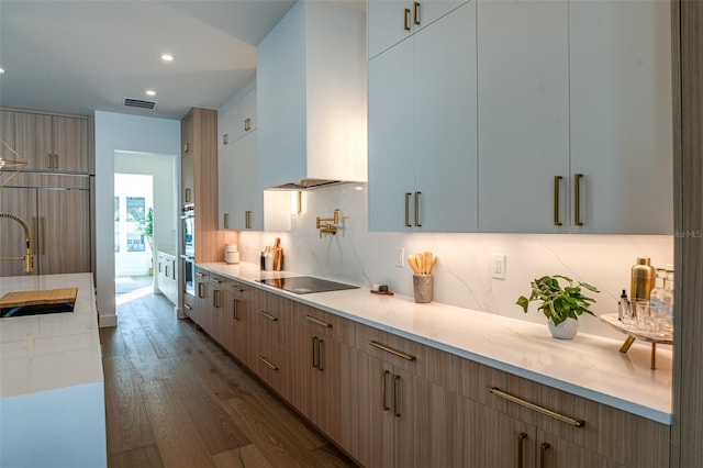 kitchen featuring backsplash, black electric stovetop, paneled built in fridge, wall chimney exhaust hood, and dark hardwood / wood-style floors