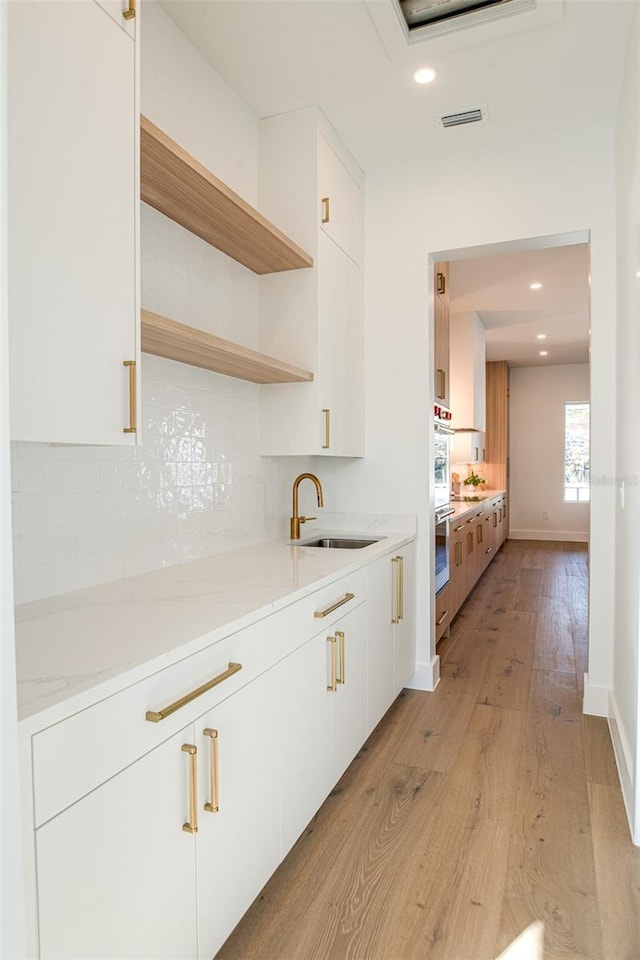 bar with decorative backsplash, light stone counters, sink, white cabinets, and light hardwood / wood-style floors