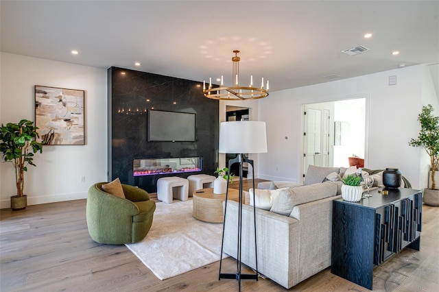 living room featuring a high end fireplace, light wood-type flooring, and an inviting chandelier