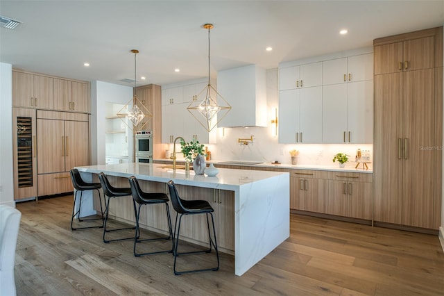 kitchen with a spacious island, sink, decorative light fixtures, light hardwood / wood-style flooring, and white cabinets