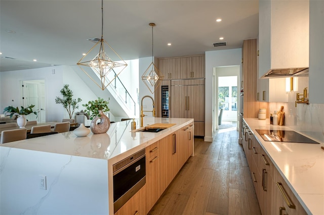 kitchen with a large island, sink, hanging light fixtures, black electric stovetop, and custom range hood