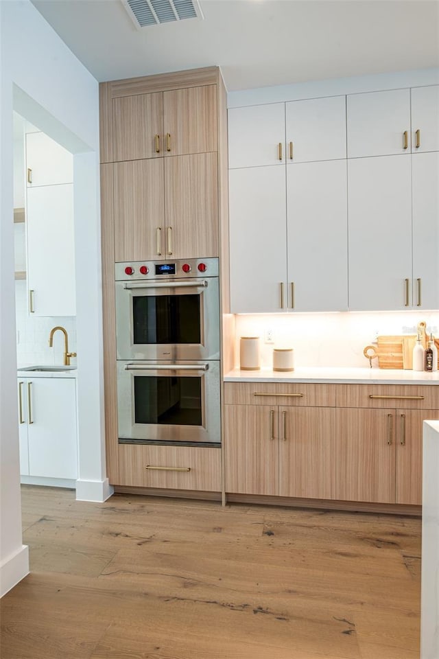 kitchen with sink, light hardwood / wood-style flooring, decorative backsplash, light brown cabinetry, and double oven