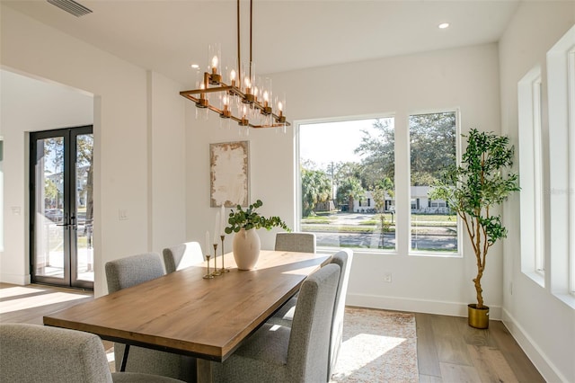 dining room with plenty of natural light, light hardwood / wood-style floors, french doors, and an inviting chandelier