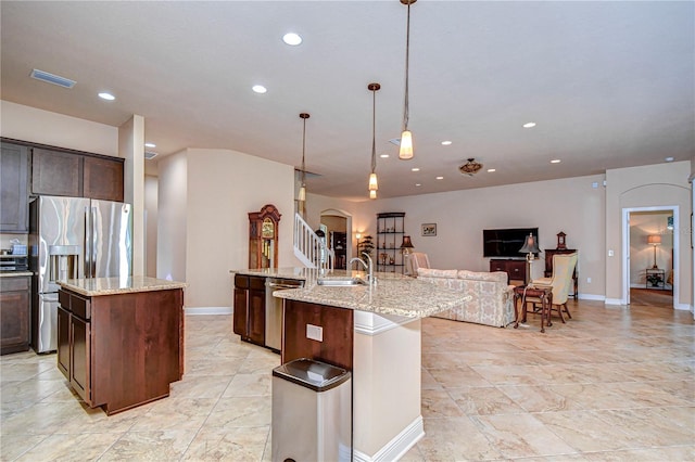 kitchen with light stone counters, appliances with stainless steel finishes, hanging light fixtures, and a kitchen island with sink