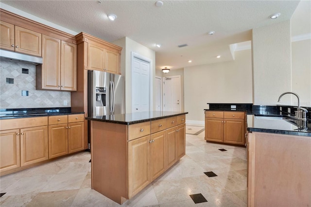 kitchen featuring dark stone countertops, a center island, stainless steel refrigerator with ice dispenser, decorative backsplash, and sink