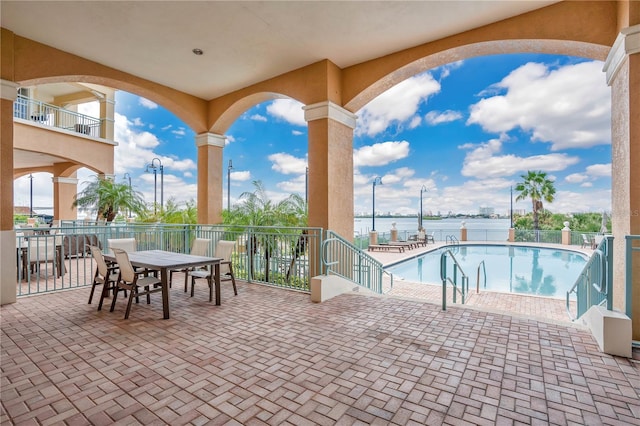 view of patio with a water view, a community pool, and a balcony