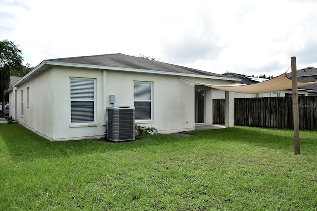 rear view of property with central AC unit and a lawn